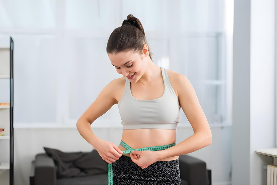 Контроль прогресса: девушка измеряет объем талии сантиметровой лентой для отслеживания изменений тела.